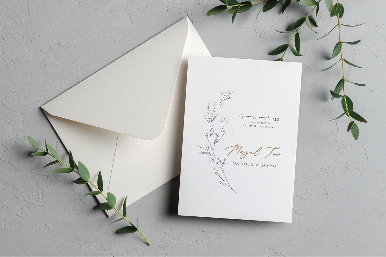 This Wispy Floral Jewish Wedding Card is a graceful way to celebrate a new marriage. The design features a delicate, climbing floral illustration alongside the timeless verse "I am my beloved's and my beloved is mine" in both Hebrew and English. For a truly premium finish, the Mazal Tov greeting is printed in a beautiful, shimmering gold foil script. Each card is printed on our signature 130lb. premium heavy ecru cardstock using professional presses to ensure a high-end, tactile feel. The inside is left completely blank, providing plenty of space for your heartfelt personal message to the couple